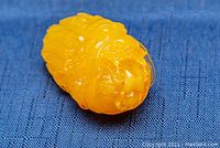 Close-up photo showing the underside and side details of the carved amber dragon pendant on a blue fabric background.