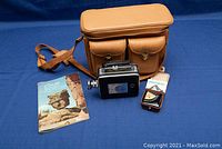Group shot of camera, light meter, manuals, and carrying case against blue background
