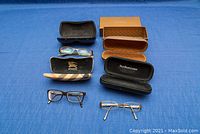 All three pairs of eyeglasses and four eyeglass cases arranged on blue fabric surface.
