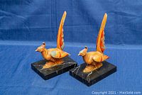 Pair of metal carved pheasant bookends on black stone bases, side view showing detailed carving and paint wear.