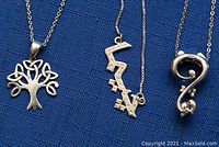 Close-up of three distinct silver pendants on chains: tree, abstract zigzag, stylized question mark.