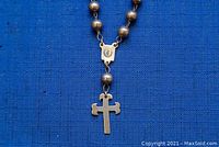 Close-up of rosary beads with cross pendant and hallmark plate on blue background