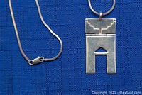 Close up of silver geometric pendant featuring rectangular shape with cutouts and etched top design alongside silver chain with lobster clasp on blue background.