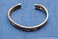 Full view of open silver cuff bangle on blue background