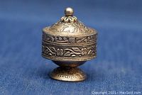 Side view of the sterling silver footed pill box showing the floral engraved design and spherical finial on lid.