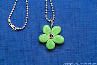 Necklace with green flower pendant displayed on blue fabric background, showing pendant details