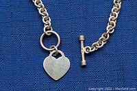 Close-up of heart-shaped charm and toggle clasp of sterling silver bracelet on blue background.