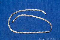 Full view of the 20-inch twisted sterling silver chain necklace laid flat on a blue fabric.
