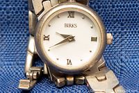 Close-up front view of Birks ladies watch showing white dial, Roman numeral markers, and silver linked band.
