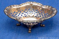 Oval sterling silver footed bowl with reticulated floral cutout designs on a blue background.