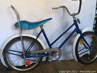 Side view of blue chopper bicycle showing frame, banana seat, chain guard, and rear tire.