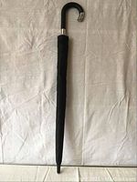 Full view of the closed black umbrella showing its length and tapered closed canopy.