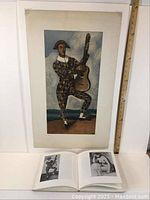 Full view of the lithograph showing the harlequin figure with guitar and an open book below illustrating similar images.