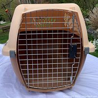 Front view of beige plastic pet carrier with metal wire door locked, showing ventilation holes on sides.