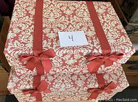 Two stacked red and white damask patterned fabric covered storage boxes with red bows, showing full front and top view.