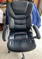 Front view of a large black office chair with padded armrests and segmented cushioned backrest, showing signs of light wear.