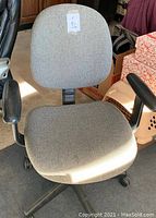Small grey cloth office chair with wheels and black armrests, showing overall condition including small fabric stains.
