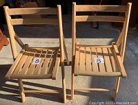 Photo showing two foldable wooden slat chairs side by side with natural wood finish and horizontal slats on seat and backrest.