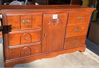 Wooden dresser in sunlight showing six drawers and a center cabinet door, with metal handles and some visible scratches.