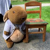 Photo of a small wooden child's chair with painted seat and ABC carved on backrest, paired with a large brown Peter Rabbit plush wearing a light shirt.