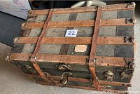 Top view of antique wooden trunk showing wood slats, leather straps, metal studs, and locking hardware with wear and damage.
