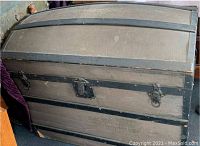 Closed view showing grey exterior with black metal bands and latches, curved dome lid.