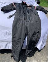 Full frontal view of vintage Arctic Cat insulated snowmobile suit lying flat, showing front zipper, snap flap, and pink accent trim on sleeves and chest logo patch.