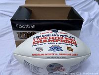 Photo of the limited edition white commemorative football with detailed printed text about the Patriots' Super Bowl XXXIX victory and original box.