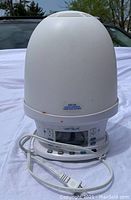 White Verilux clock with snooze and light, power cord attached, shown outdoors on white fabric background.