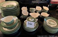 Set of dishware including stacked green and white dinner plates, smaller plates, various sizes of bowls, creamer, sugar bowl with lid, and gravy boat.