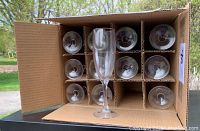 Top view inside the box showing 12 clear glass champagne flutes arranged upright in cardboard dividers.