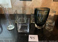 Photo showing 6 glass vases of different shapes and sizes on a countertop, labeled "45".