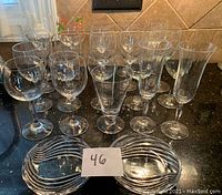 Photo showing 20 assorted wine glasses of various shapes and 2 matching oval clear glass candy dishes placed on kitchen counter.