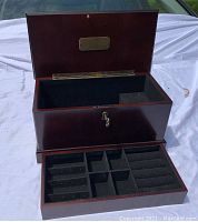 Wooden jewelry box open showing black velvet-lined interior with multiple compartments for jewelry storage.