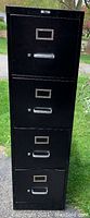 Full view of black metal 4-drawer file cabinet outdoors showing general condition and drawer handles.