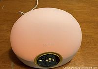 Photo of round Lume light alarm clock glowing softly with digital clock display and touch buttons on base.