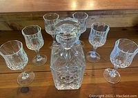 Crystal decanter with stopper and six matching crystal stemmed glasses on wooden surface.