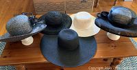 Five hats arranged on wooden table; two appear fancy with decorative elements, three are more casual and beach-appropriate.