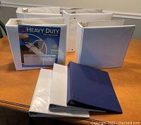 Seven large 3-ring binders on a table, six white and one navy blue, with one binder labeled Heavy Duty One Touch EZD rings.