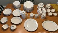 Overview photo showing the complete set of white china with silver trim spread on a wooden table. Includes all plates, bowls, platters, and serving dishes mentioned.