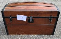 Front view of antique dome top wooden trunk with black metal hardware and central lock. Shows wood panels and metal reinforcements on corners and edges.