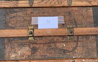 Close-up top view of antique trunk showing wood grain, metal hardware, and taped paper with number 73.