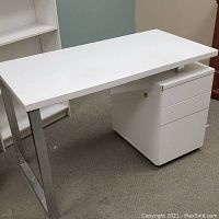 White contemporary desk with rectangular top, chrome legs on one side and built-in filing cabinet on the other.