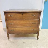 Front view of the closed cedar chest showing three drawer fronts with ornate handles, keyhole, and curved legs.