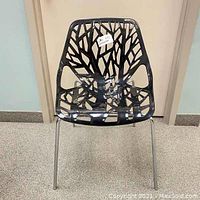 Front view of black chair with tree branch cut-out design and chrome legs visible.
