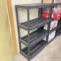 Full view of assembled black 4 level plastic shelf against wall showing structure and shelves.