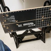 Top of Black and Decker Workmate 225 showing black wooden surface with printed ruler, grid and multiple holes with some wear and rough edges.