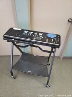 Front side view of Mobilfold black metal folding table with graphics on top displaying shirt fit guide and brand information. Table is on caster wheels.