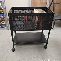 Front view of black metal mesh rolling file holder showing the upper compartment with hanging file folders and lower shelf