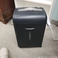Front view of the black Insignia paper shredder showing its rectangular shape and wheel base.